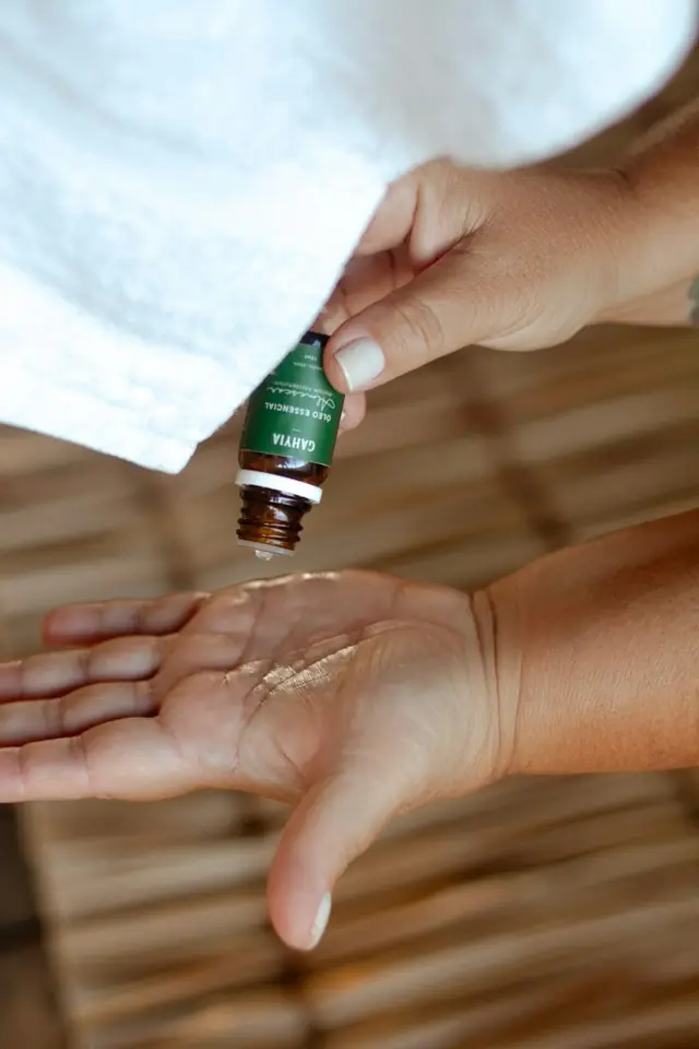 Óleo essencial sendo pingado na palma da mão, com uma toalha branca ao lado